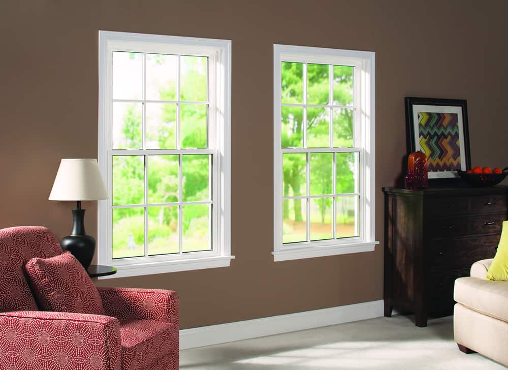 Image shows an interior with two white double hung windows on a brown wall with white trim. A red chair and lamp sit to the side of the windows.