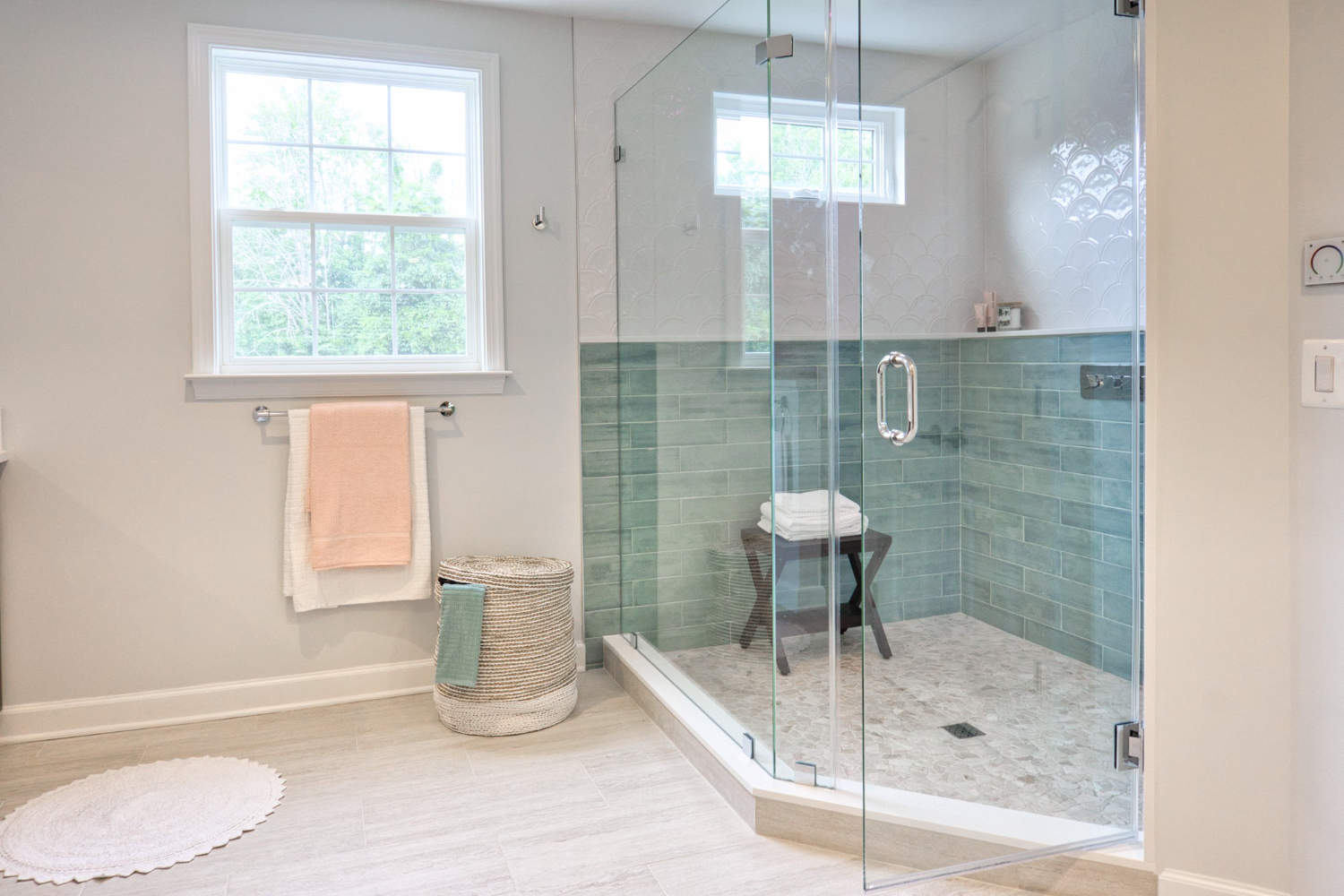 Image shows a bright, modern bathroom with light colored walls and a large walk in shower. Light pours through a window into the room. 