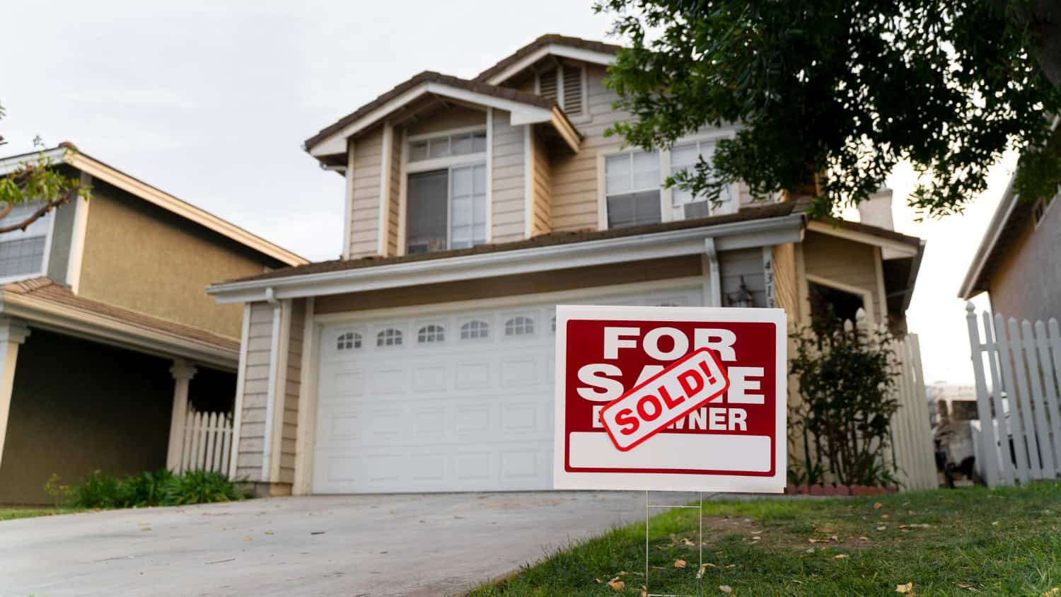 Image shows the exterior of a home with a "sold" sign in front next to the driveway.