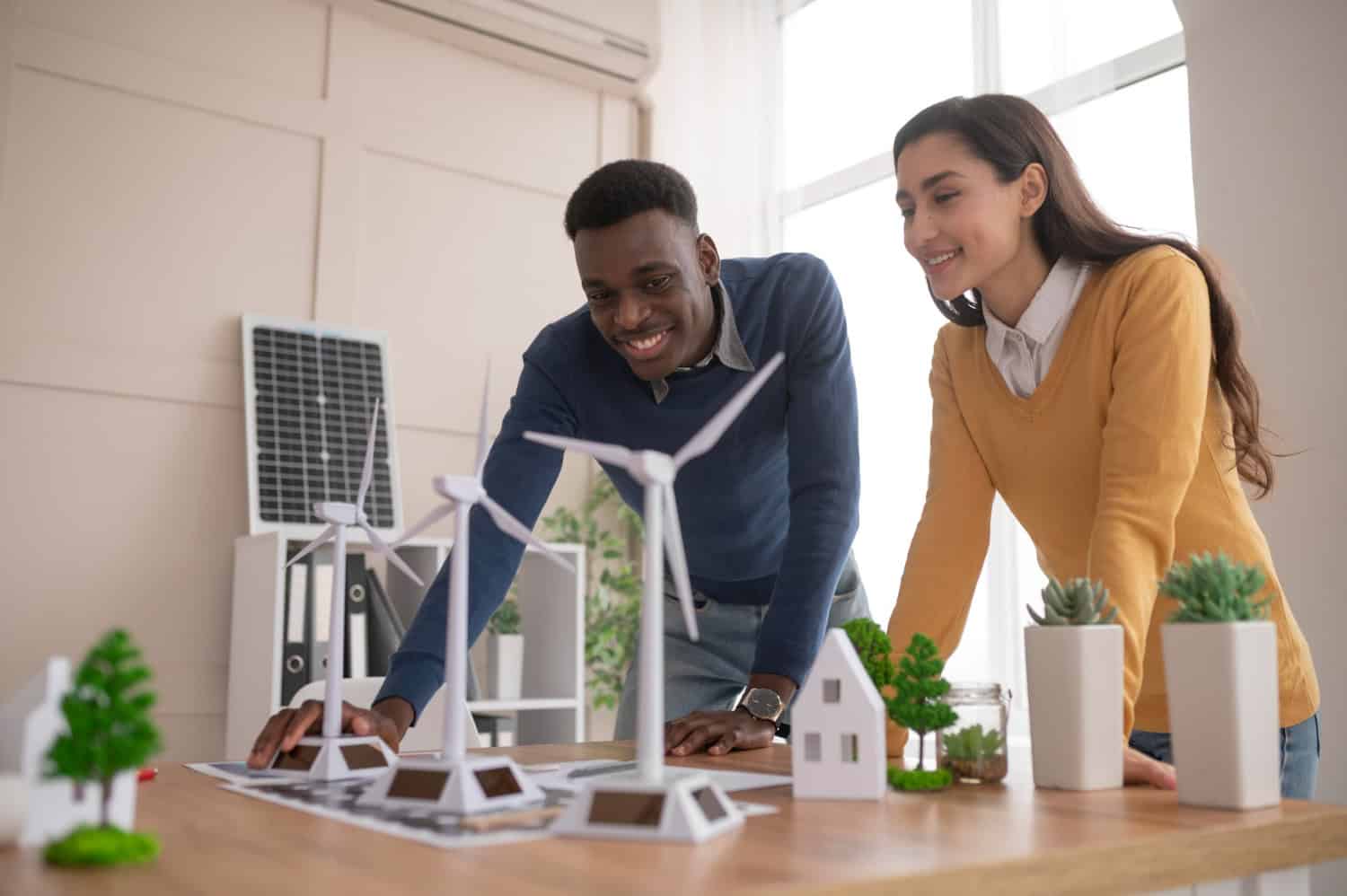 Image shows a man and a woman leaning on a table with a model of wind turbines and homes.