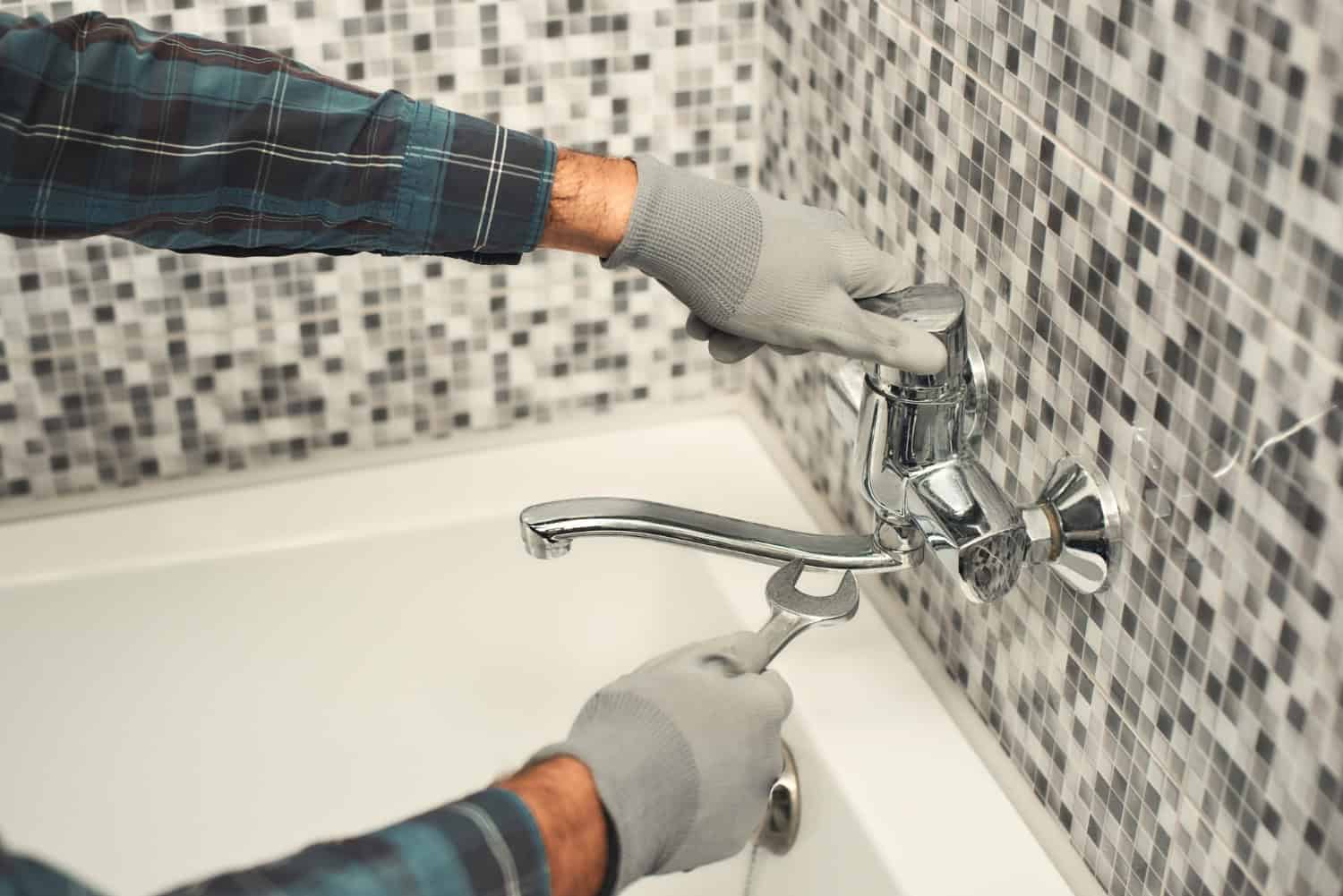 A professional works on installing a new bathtub faucet on a black and white tiled bathroom wall.