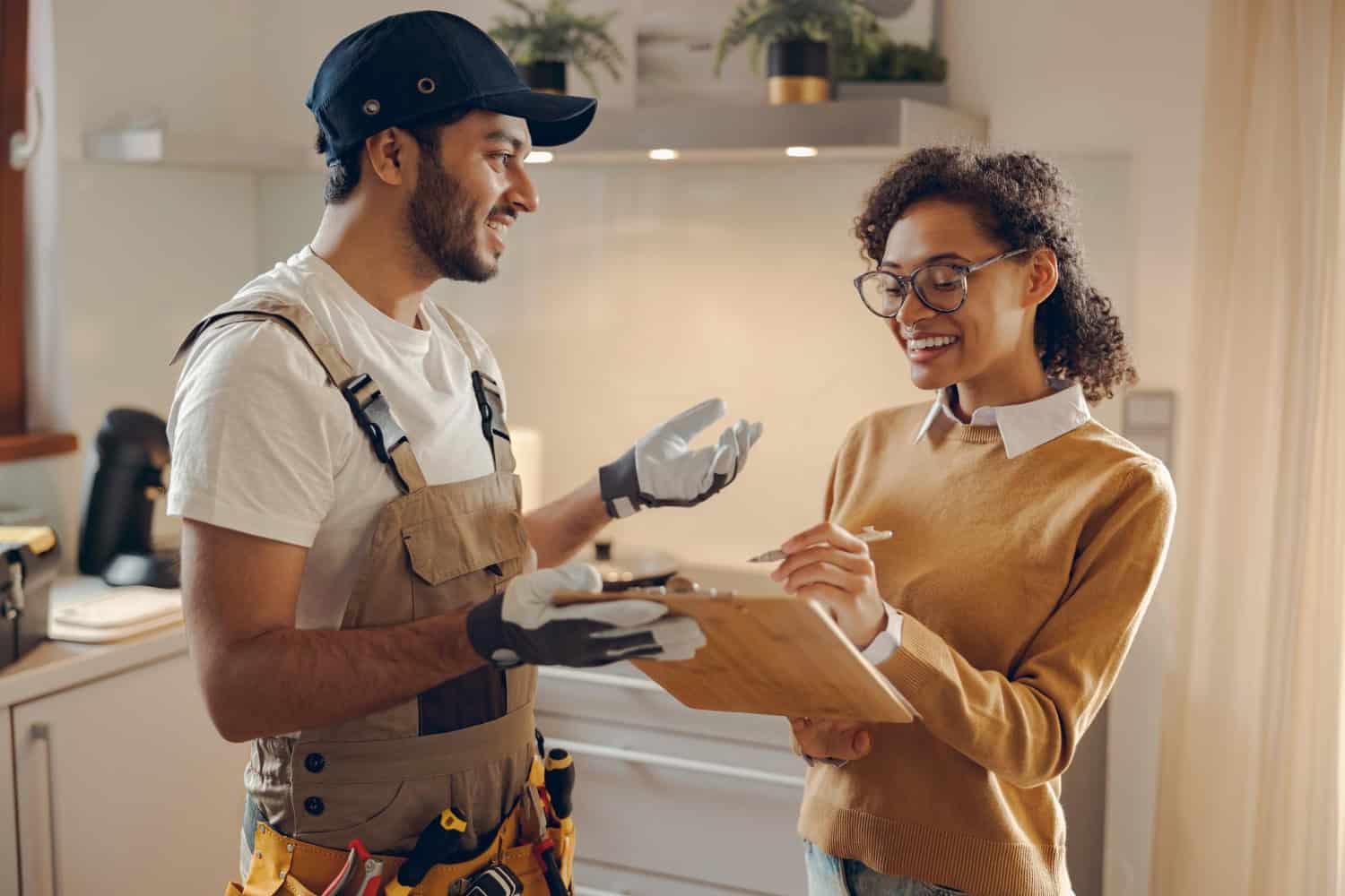 A woman meets with a home contractor in her kitchen. She is signing a document on a clip board, smiling.